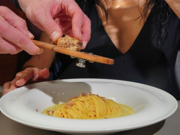 person shaving white truffle onto a plate of pasta