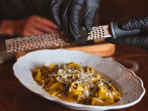 black truffle being grated over a pasta dish